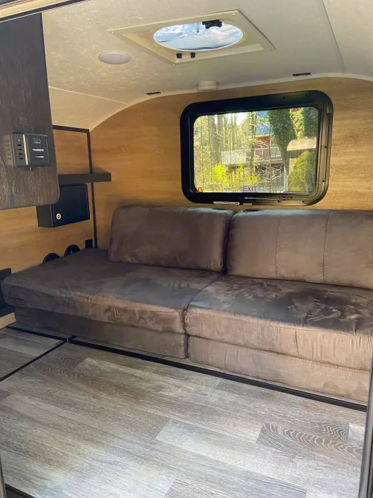 Cozy rv rental interior with a versatile sofa bed, wood-look walls, and bright ceiling vent, ideal for compact living.. Bushwacker 10SS 2021