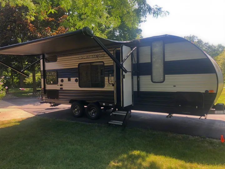Spacious Grey Wolf rv rental travel trailer, awning extended, parked on a driveway amidst green trees. Perfect for camping trips!. Forest River Cherokee Grey Wolf 22MKSE 2020