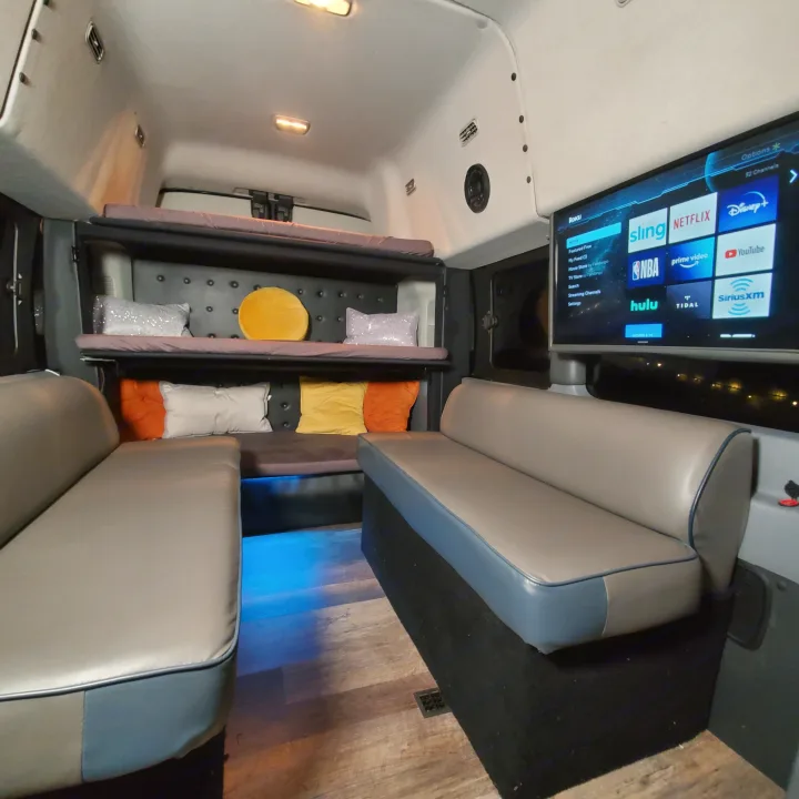 Inside an RV rental: plush seating, bunk beds, and a TV with streaming apps like Netflix and Hulu for your journey.. Ford Custom Transit 2017