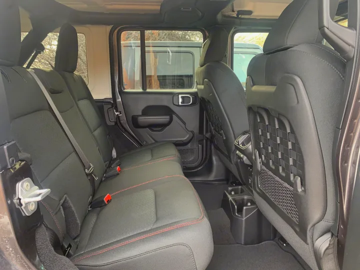 Inside a roomy RV rental: comfortable black rear seats with red stitching, secure seatbelts, convenient cup holders, and storage pockets.. Jeep Gladiator Unlimited 2020