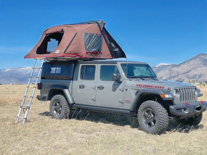 Overland camping setup: Gray Jeep Gladiator with rooftop tent for an outdoor RV rental adventure in a scenic mountain setting.. Jeep Gladiator Unlimited 2020
