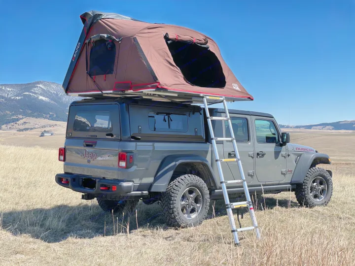 This gray Jeep Gladiator with a deployed brown rooftop tent is ready for your overland RV rental adventure in the mountains.. Jeep Gladiator Unlimited 2020