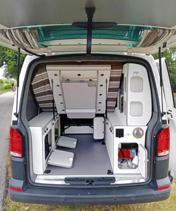 Rear view of an **rv rental** camper van with a modular interior. Features include a convertible bed/table, storage, and water system.. Volkswagen Transporter T6 2021
