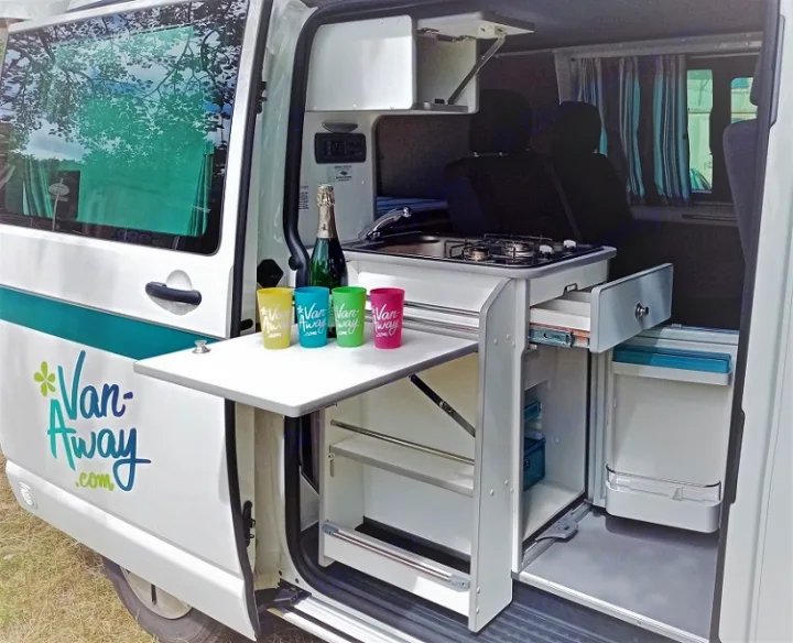 An RV rental's clever design: a campervan kitchen with stove, sink, fridge, and a pull-out table for easy outdoor dining.. Volkswagen Transporter T6 2021