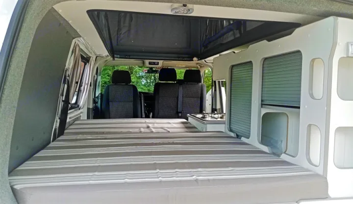 Cozy RV rental camper van interior with a bed, kitchen hob, and storage, designed for comfortable road trip adventures.. Volkswagen Transporter T6 2021