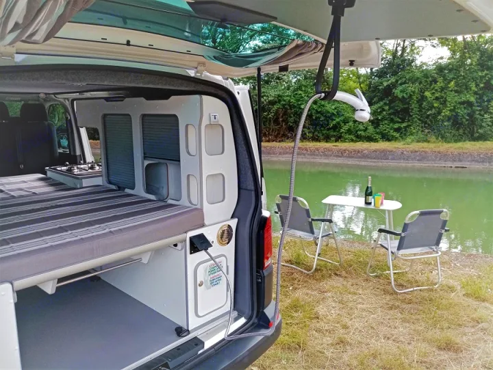 Compact RV rental: interior with bed & kitchen, plus outdoor shower and dining by a tranquil canal.. Volkswagen Transporter T6 2021