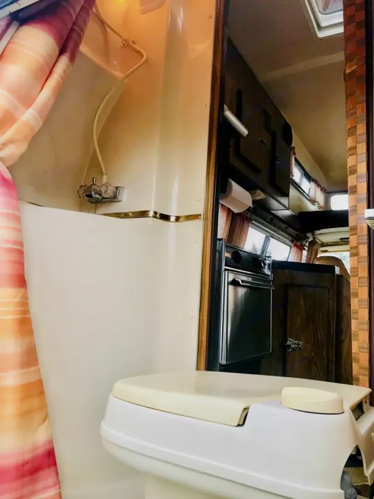 Explore a functional RV rental interior: compact bathroom with shower/toilet and a glimpse of the kitchen's oven.. Frontier Other 1979