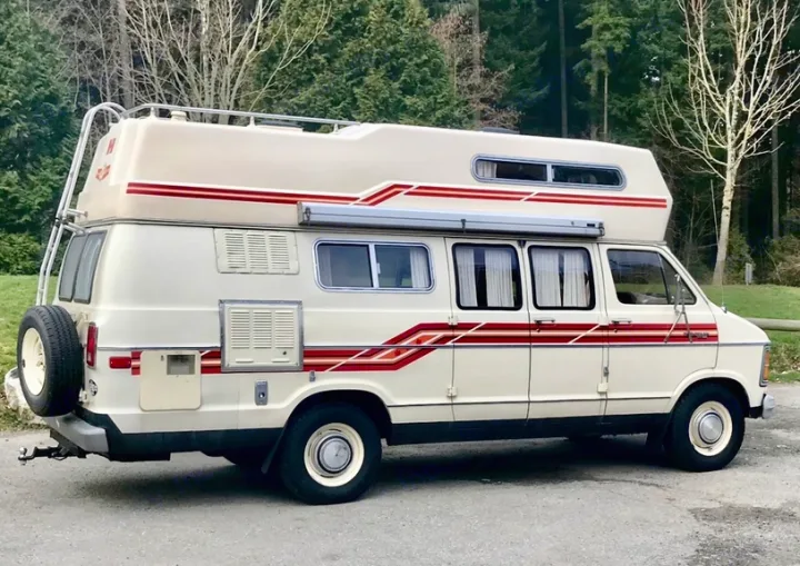 This vintage Dodge camper van, featuring a cream body with red stripes, roof rack, and ladder, could be a classic RV rental.. Frontier Other 1979