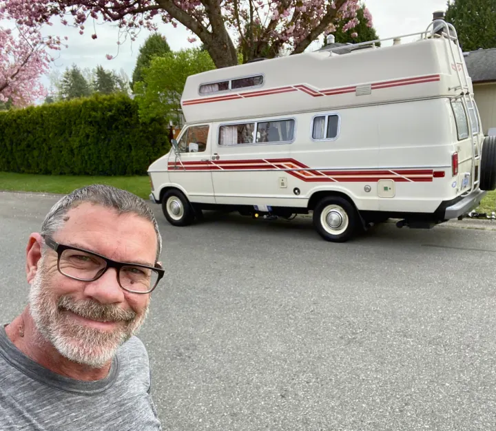 Smiling man with his classic white RV rental, a vintage camper van, parked on a street.. Frontier Other 1979