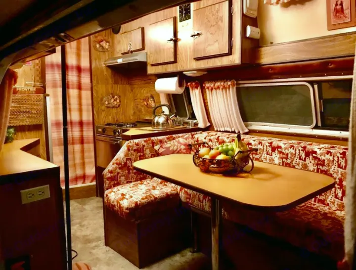 Experience a retro rv rental: cozy vintage camper interior with full kitchen, dining, and warm wood accents. Perfect for travel.. Frontier Other 1979