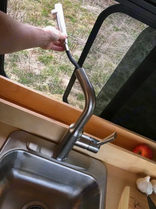 RV rental kitchen: Hand extends pull-down faucet sprayer out window, showing compact sink, counter with apple & garlic.. Ram Promaster 2021