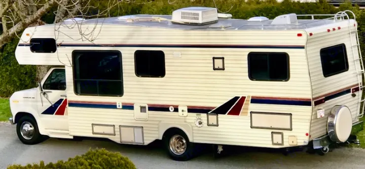 Cream-colored Class C RV, great for rv rental, road trips, and camping. Features a side stripe and roof AC.. Ford Econoline 1988