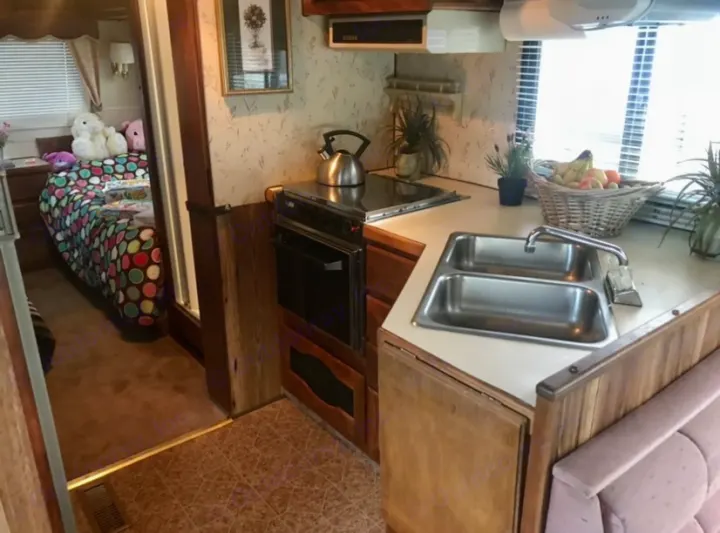 Cozy RV rental interior featuring a full kitchen with sink, stovetop, and oven, plus a bright bedroom in the back.. Ford Econoline 1988