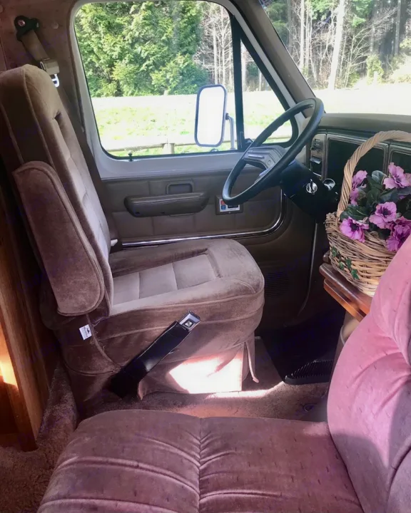 Interior of an **rv rental** showing the driver's seat, steering wheel, and passenger area with a flower basket. Ready for travel.. Ford Econoline 1988