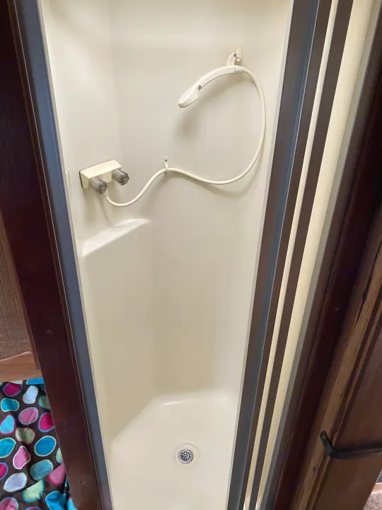Compact beige shower stall inside an RV rental, featuring a handheld showerhead, faucet controls, and floor drain.. Ford Econoline 1988