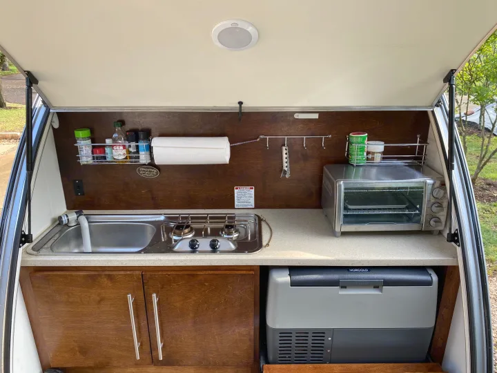 Compact RV rental outdoor kitchen with sink, stove, toaster oven, and portable fridge.. Little Guy NuCamp 2015