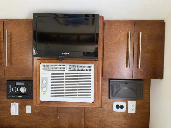 RV rental interior setup: compact TV, AC unit, stereo, and power outlets integrated into sleek wooden cabinetry.. Little Guy NuCamp 2015
