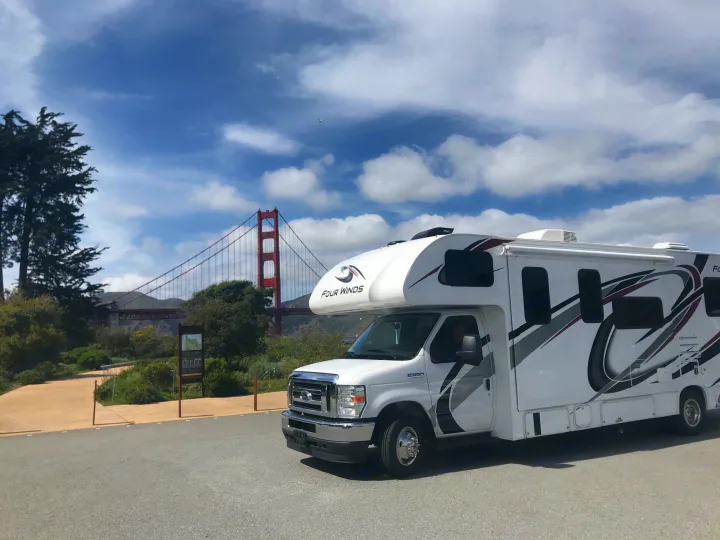 A white RV rental poses in front of San Francisco's Golden Gate Bridge under a clear, cloudy sky. Iconic travel.. Thor Four Winds 2021