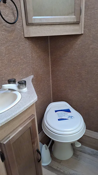 Compact RV rental bathroom featuring a Dometic toilet, sink, & cabinetry, showing essential amenities for travel.. Coachmen Freelander 2015