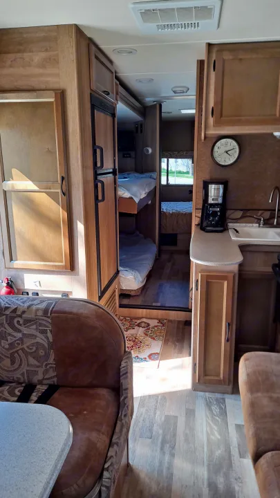 Cozy RV rental interior with kitchen, living space, and bedroom beyond. Features light wood cabinetry, laminate flooring, and sunlight.. Coachmen Freelander 2015