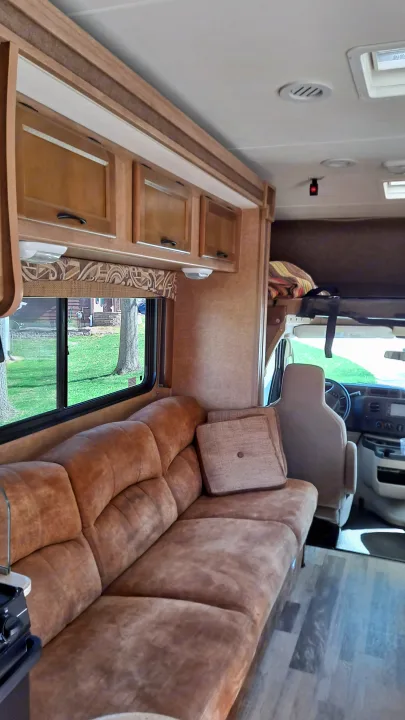 Interior of an RV rental, showing a comfortable brown sofa, wooden cabinets, and the front cockpit. Ready for adventure.. Coachmen Freelander 2015