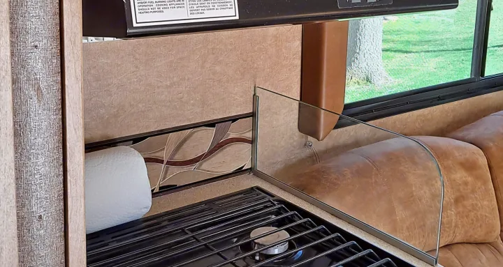 RV rental interior: A gas stove with metal grates, a clear glass splash guard, and paper towels on the counter.. Coachmen Freelander 2015
