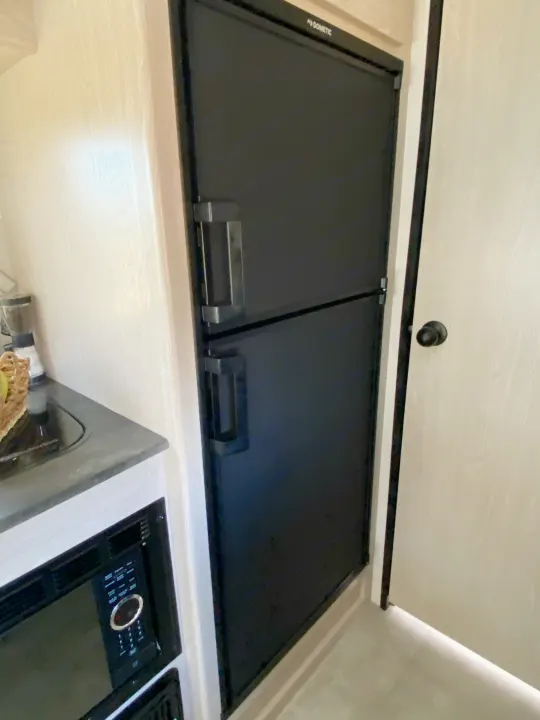 Compact kitchen in an RV rental, featuring a black Dometic refrigerator/freezer and microwave.. Coachmen Apex 2021