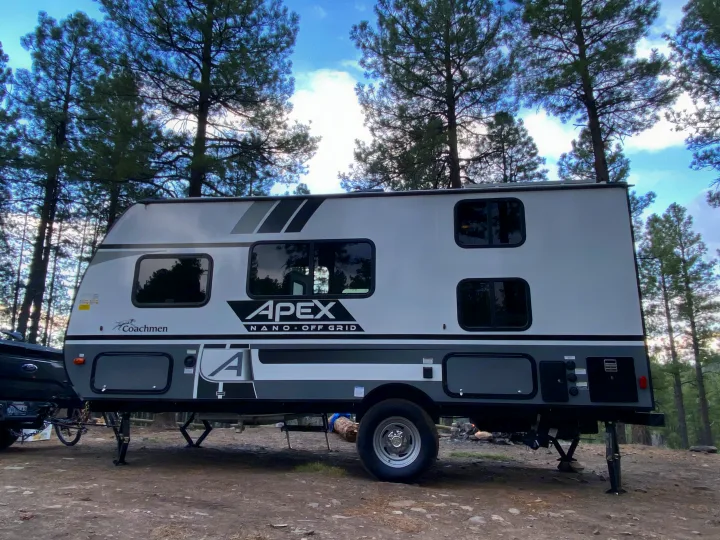 Experience nature with this APEX travel trailer rv rental at a serene pine tree campsite, perfect for off-grid adventures.. Coachmen Apex 2021