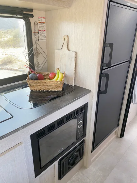 Compact RV rental kitchen features a stovetop, Greystone microwave, Dometic refrigerator, and fresh fruit. Your mobile cooking space.. Coachmen Apex 2021