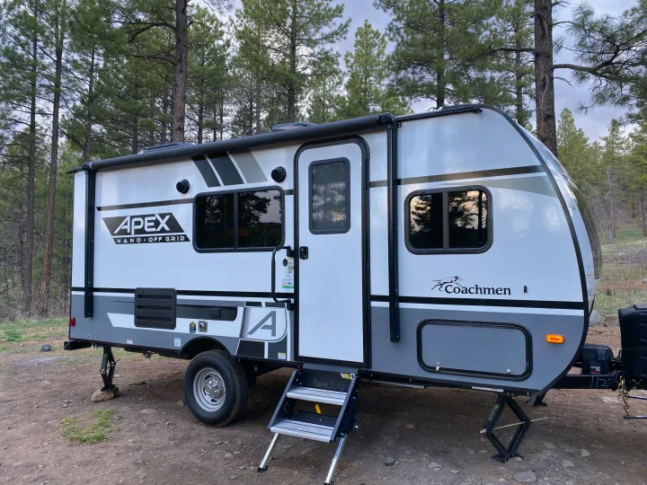 An off-grid ready Apex Nano travel trailer, perfect for an rv rental, nestled in a pine forest with stabilization jacks down.. Coachmen Apex 2021