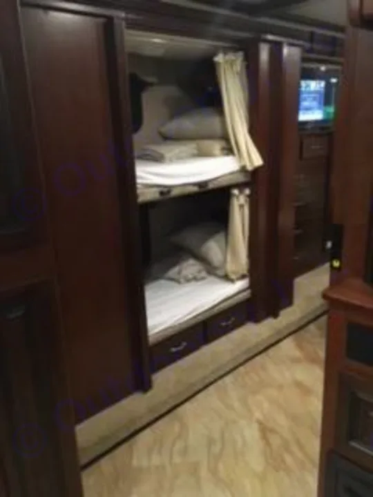 Dark wood bunk beds with white linens in a spacious RV rental interior. Ideal for motorhome family trips.. Holiday Rambler Vacationer 2017