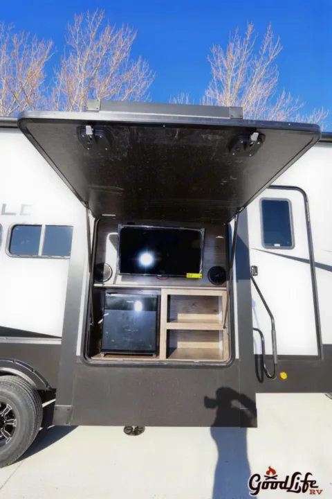 This RV rental's outdoor entertainment center features a TV, speakers, mini-fridge, and shelving, ideal for camping.. Alliance RV Valor 40V13 2021