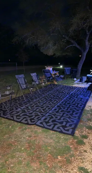 Nighttime RV rental setup: comfy chairs, large mat, and picnic table under the stars for an inviting outdoor living space.. Forest River Wildwood 2021