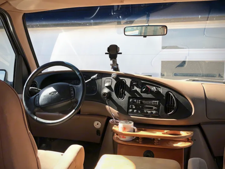RV rental interior: Driver's seat view of the dashboard, steering wheel, and custom wooden tray in a campervan.. Ford Econoline 1997