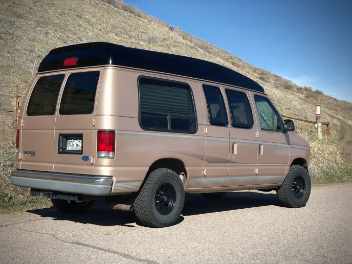 Tan Ford Econoline high-top camper van, an ideal RV rental for exploring scenic Colorado trails.. Ford Econoline 1997