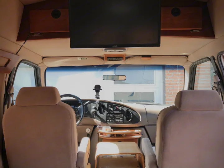 Interior of an RV rental, showing the front cabin with two tan seats, dashboard, and an overhead TV.. Ford Econoline 1997