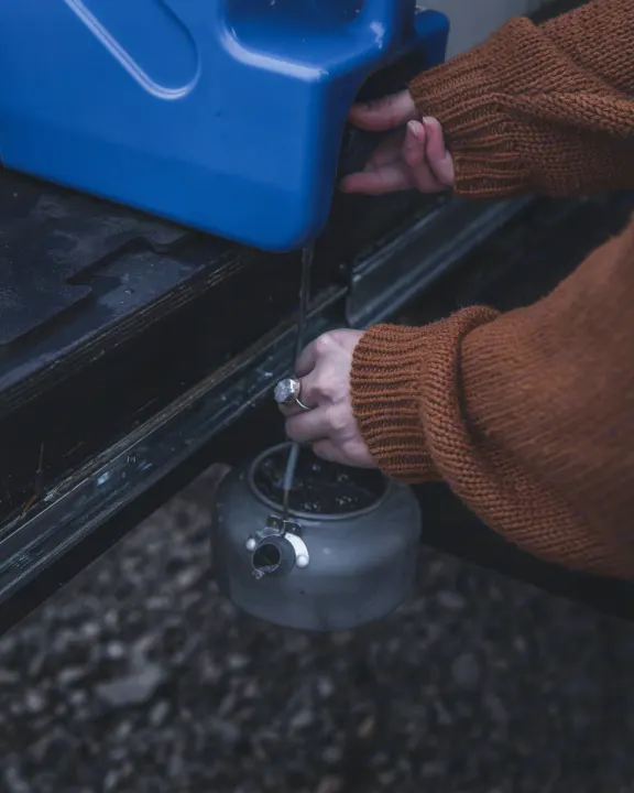 Hands fill a kettle from a blue water tank, essential for an RV rental trip or camping adventure.. Toyota 4Runner 2021