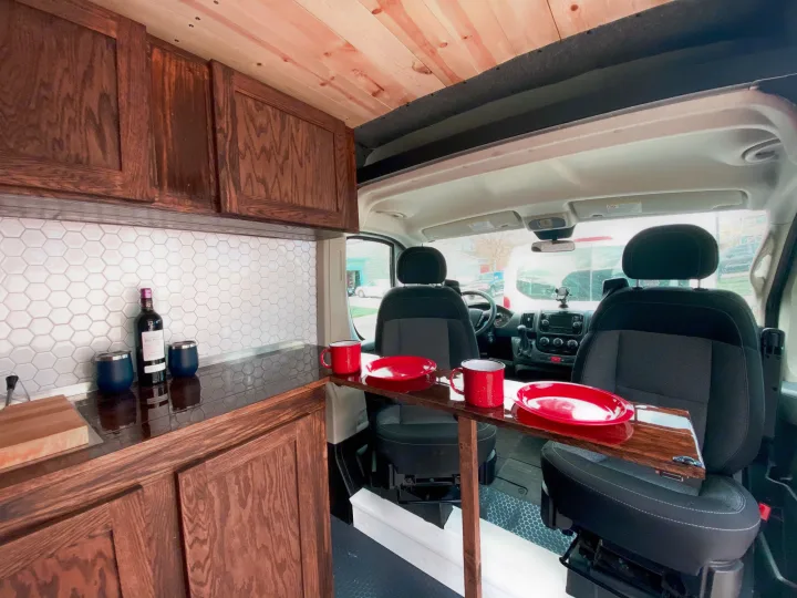 RV rental: Custom van interior features a wooden kitchen, hexagonal tile backsplash, and front seats with a built-in table.. Ram Promaster 2020