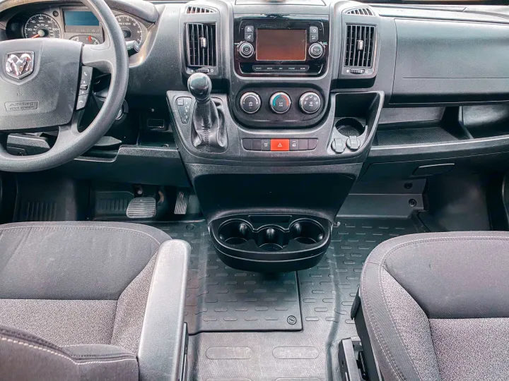 Inside an RV rental: a detailed view of the dashboard, steering wheel, and cabin controls with clean floor mats.. Ram Promaster 2020