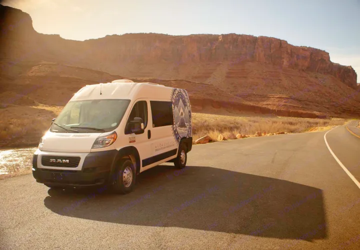 White **rv rental** camper van on a desert road, bathed in warm light, surrounded by majestic red rock canyons and a river.. Ram Promaster 2021