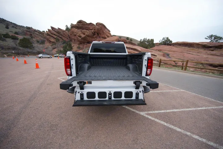 White GMC pickup truck's multi-function tailgate open, at scenic red rocks. Ready for gear & trips, similar to an RV rental for outdoor adventures.. GMC Sierra 2500HD 2021