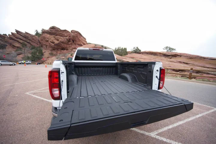 White GMC pickup truck's open bed & tailgate, ready for RV rental supplies in a mountain park.. GMC Sierra 2500HD 2021