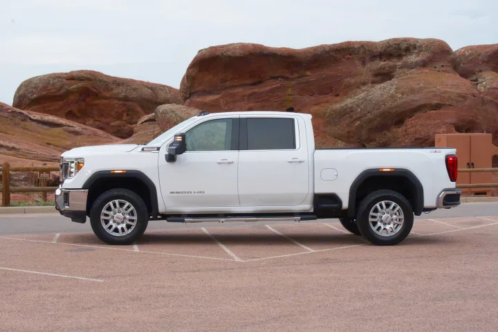 White GMC 2500HD heavy-duty truck parked near red rocks, ideal for an RV rental trip with its towing capacity.. GMC Sierra 2500HD 2021