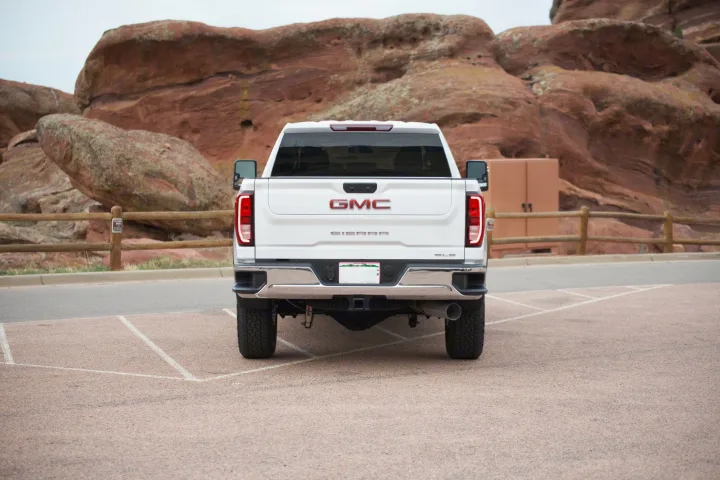 Rear view of a white GMC Sierra pickup truck parked near red rock formations, ready for your next rv rental adventure.. GMC Sierra 2500HD 2021