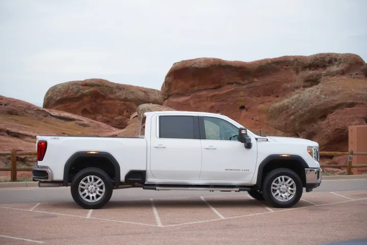 A white GMC Sierra 2500 HD pickup truck parked by red rock formations. A rugged vehicle for adventures, or to tow your RV rental.. GMC Sierra 2500HD 2021