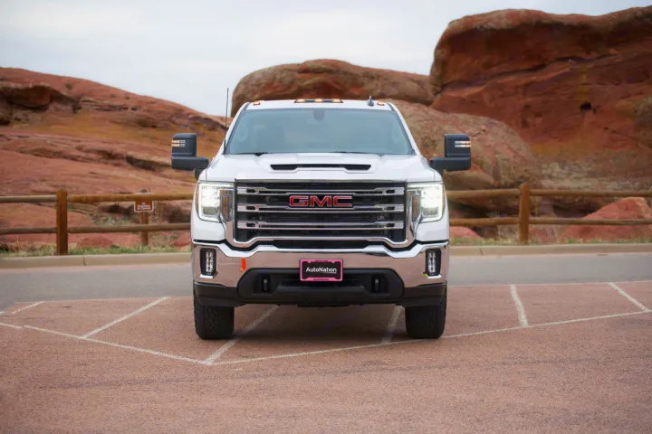 Front view of a white GMC pickup truck parked on asphalt, with large red rock formations behind. Ideal for **rv rental** adventures.. GMC Sierra 2500HD 2021