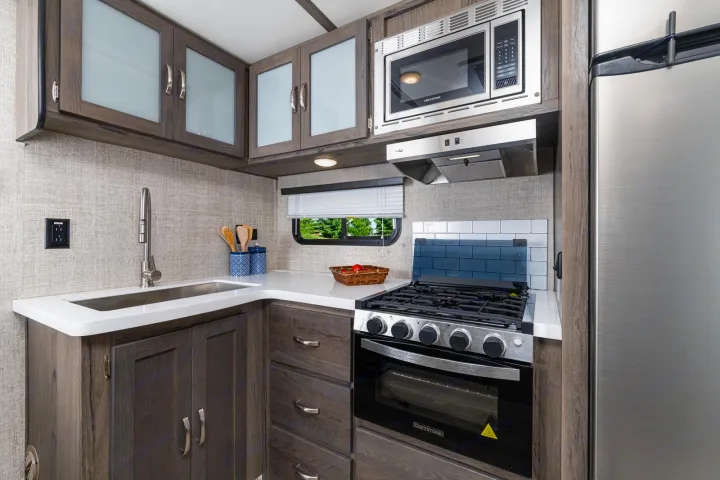 Modern and compact RV rental kitchen with essential appliances: microwave, stove/oven, fridge, sink, and ample cabinet space.. Gulf Stream Envision 2021