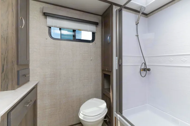 RV rental bathroom: compact design with white toilet, shower, and wooden vanity. Functional interior for travel.. Gulf Stream Envision 2021