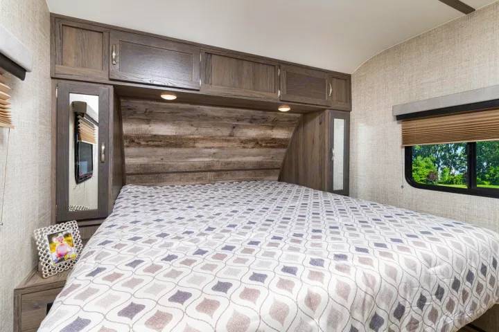 RV rental bedroom features comfy bed, wood-paneled headboard & overhead cabinets, plus a window with nature views.. Gulf Stream Envision 2021