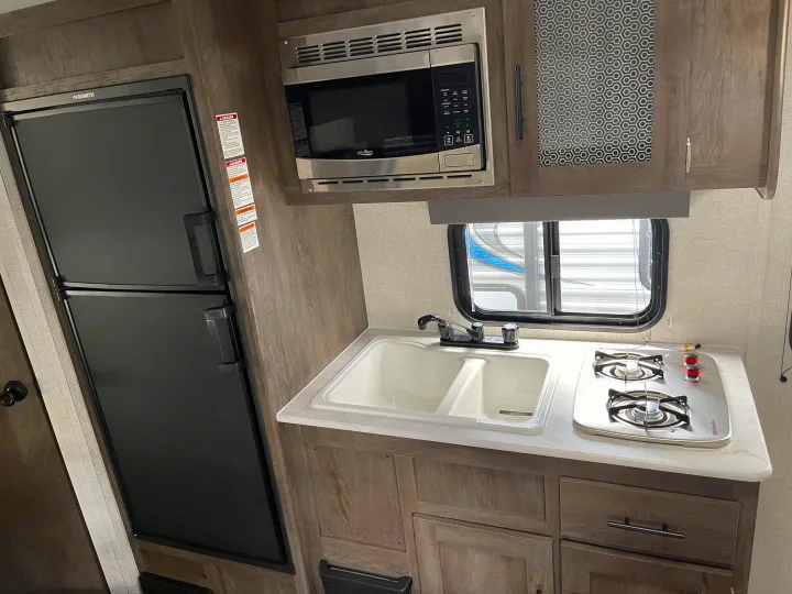 An RV rental kitchen with a black Dometic fridge, High Pointe microwave, double sink, and two-burner Suburban stove.. Forest River Salem 179 2021
